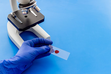 Blood testing with microscope in laboratory. Sample in hands on blue background copy space
