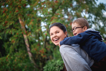 A small child 3-4 years old rides his mother, plays a horse, laugh, emotions. Shot on an old soviet manual focus lens with spinning unusual bokeh.
