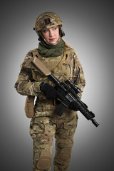 Fototapeta premium Female soldier in tactical black uniform with rifle. Shot in studio. Isolated with clipping path on grey background