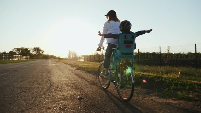 Mom with her little son are riding a bike on the road at sunset, rear view, slow-motion