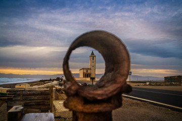 Fototapeta premium The iconic church of San Miguel seen through rusty fishing gear at sunset, Las Salinas, Cabo de Gata-Níjar Natural Park, Almería, Andalusia, Spain