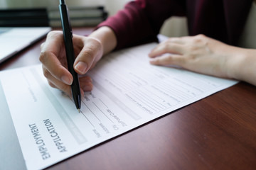 Naklejka premium Woman Hand holding pen to filling application company for employment on wood table. Concept of recruitment, unemployed, applying for work.