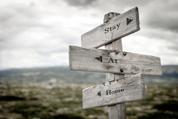 stay at home text engraved on old wooden signpost outdoors in nature. Quotes, words and illustration concept.