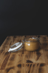 Jar of peanut butter on a wooden board, black background