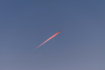 A long rose red sunset trail of jet plane on blue sky.