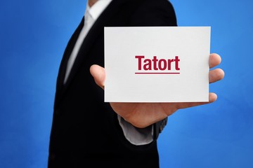 Tatort. Anwalt hält Karte in der Hand. Beschriftung auf Schild zeigt Begriff. Hintergrund blau. Recht, Gesetz, Rechtsprechung