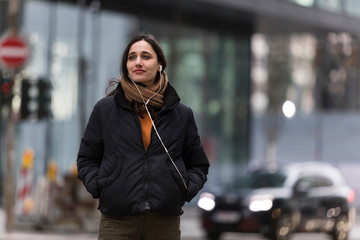 Young Indian woman listening to earphones on street looking away with head turned.