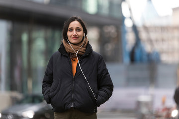 Young urbanite woman posing on street listening to earphones.