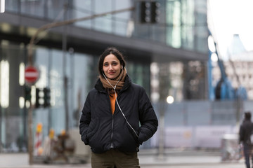 Fototapeta premium Young woman wearing jacket and listening to earphones smiling sincerely on city street.