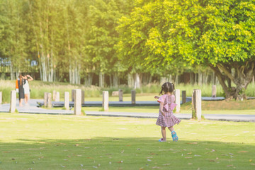 A little girl in a pink skirt enjoys a relaxing time playing on the green lawn at the public park in the evening.