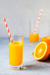 Tall glass of tasty freshly squeezed orange juice standing on table on hot summer day with halved fresh orange. Vertical layout