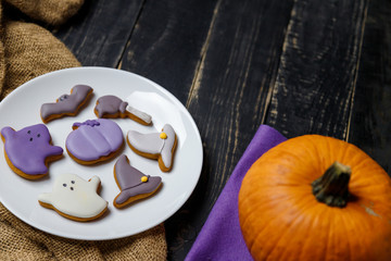 Pumpkin and Halloween cookies on white plate, sackcloth on black wooden background. Hallooween trick or treat concept. Copy space.