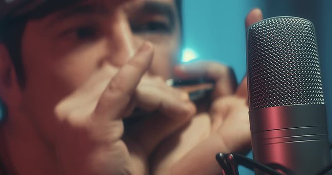 Close-up Musician in headphones playing on harmonica at home sitting on floor at evening time. Music hobby, Create own songs, learning online. Social distancing, 4K video
