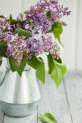 metal watering can with a bouquet of lilac on a wooden background near the window