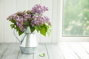 metal watering can with a bouquet of lilac on a wooden background near the window