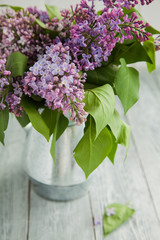 metal watering can with a bouquet of lilac on a wooden background near the window