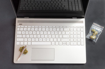 Black table with cannabis buds and big marijuana joint on laptop. Concept of weed and technology.