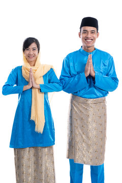 Muslim Malay Couple With Greeting Gesture Over White Background. Wishing You Eid Mubarak