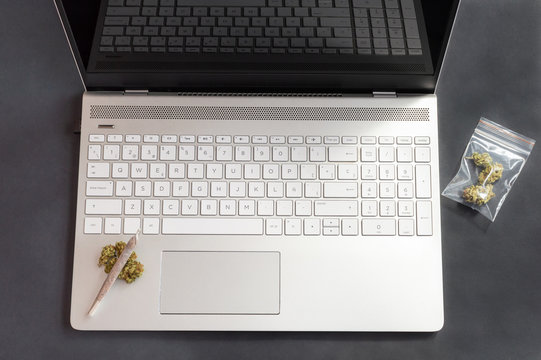 Black Table With Cannabis Buds And Big Marijuana Joint On Laptop. Concept Of Weed And Technology.