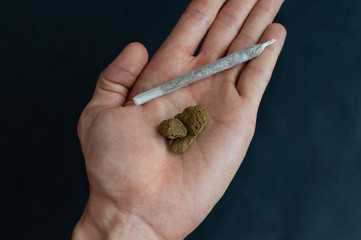 Top view of a hand holding a piece of high quality hashish and a big joint. Hand with hash joint isolated on black background.