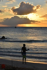 Fototapeta premium silhouette of boy at the beach with magnificent sunset and clouds