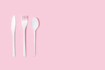 Cuchillo, tenedor y cuchara de pl&aacute;stico blanco desechable sobre fondo rosa liso y aislado. Vista superior. Copy space