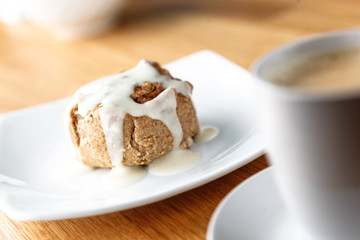 Cinnamon Bun with Icing and coffee cappucino ready to eat on a white plate with a white mug