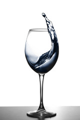 a splash of water in a glass wine glass. water splash in glass on glowing background. transparent liquid splashing in wine glass. Food, object.