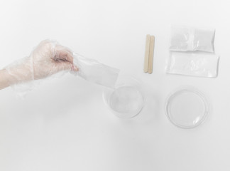 Close up of medical experiments. transparent jar, three pockets with reagents, medical gloves on isolated light background. Experiments for kids. Selective focus