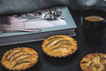 Apple tartlets, a coffee and a book on a black table