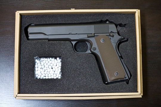 Strikeball pistol with bb bullets in a cardboard box on a glossy desk. Concept of weapon presentations
