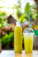 Ready to drink sugarcane juice in plastic bottles and glasses on the wooden floor there is a bokeh backdrop.