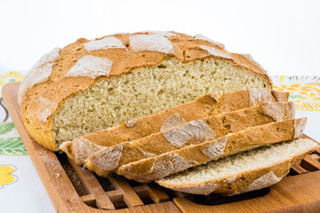 Freshly baked homemade bread on bread board half sliced to pieces.