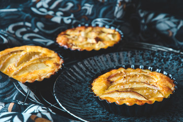 Three baked apple tartlets in black tart dishes on a black plate