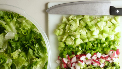 A Bowl of Lettuce Next to a Cutting Board with a Knife and Chopped Vegetables, Healthy Salad Preparations, Making a Salad