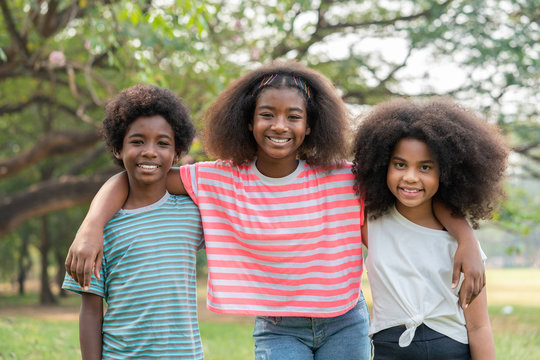 African American young girl smiling and  hugging with friends boy and girl in the park