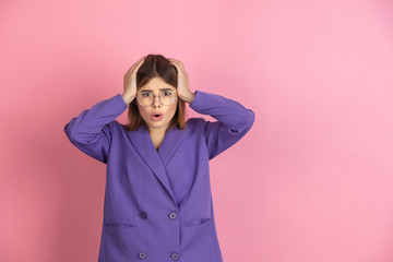 Shocked holding head. Caucasian young woman's portrait isolated on pink studio background. Beautiful female model in purple jacket. Concept of human emotions, facial expression, sales, ad. Copyspace.