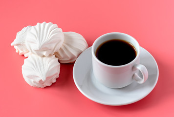 a cup of strong aromatic coffee and and a delicate white vanilla marshmallow on a pink background. place for text