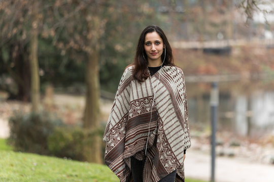 Young middle eastern woman modeling poncho in public park during autumn.