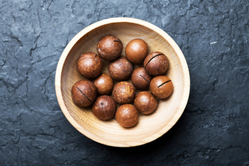Dried organic Macadamia nuts in wooden bowl closeup. Studio macro shoot. Black concrete background