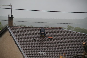 Man replacing roof tile during a storm