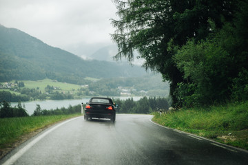 photo of a black car driving on a country road in the rain