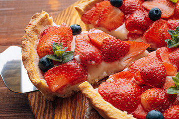 quiche with lime zest on which sliced strawberries with blueberries and fresh mint leaves on a wooden table. one slice is cut out of the pie and it is ready to serve.