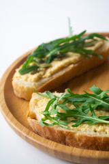 Sandwich of toasted bread slices with classic chickpea hummus spread, roasted pumpkin seeds and fresh arugula