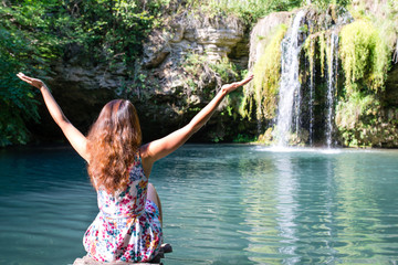 girl sitting in front of a waterfall with arms outstretched