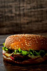 Burger on a dark wooden board. Cheeseburger with cutlet and herbs on black background. Food with contrasting dramatic light. Bun closeup.