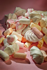 Lots of sweets on a pink background. White with orange marshmallows and bize close up.