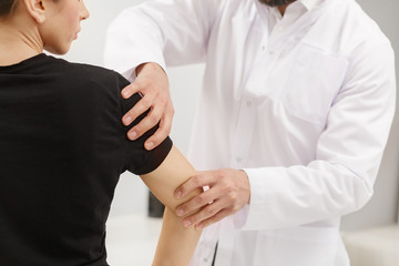 Male doctor examining female patient suffering from elbow pain. Medical exam. Chiropractic,...