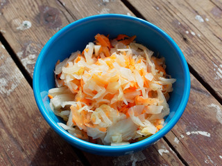 Sauerkraut with carrots in a blue plate, wooden background.