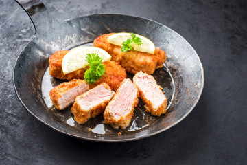 Traditionelles frittiertes Kalbssteak mit Zitronen Scheiben und Kräuter angeboten als closeup in einer rustikalengußeisernen Pfanne